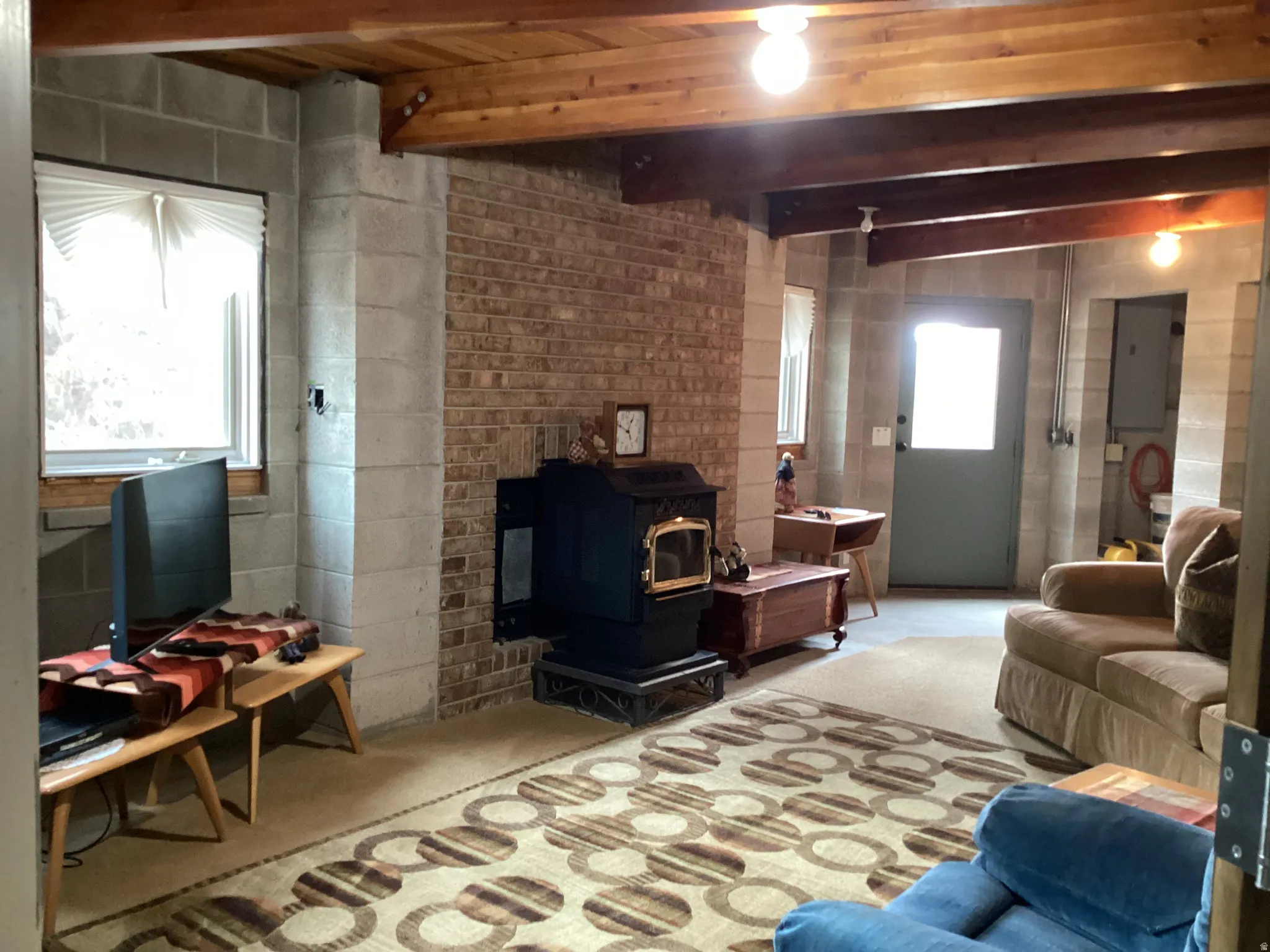 Living area with a wood stove, beamed ceiling, concrete block wall, and concrete floors