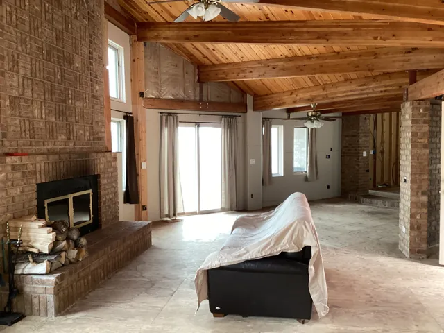 Living area with a ceiling fan, a fireplace, healthy amount of natural light, brick wall, and a high wooden beamed ceiling