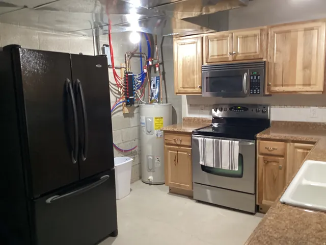 Kitchen with stainless steel appliances, water heater, concrete floors, and light wood finish cabinetry