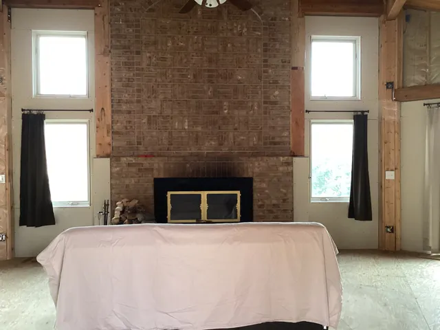 Bedroom with a large fireplace, a high ceiling, multiple windows, and ceiling fan