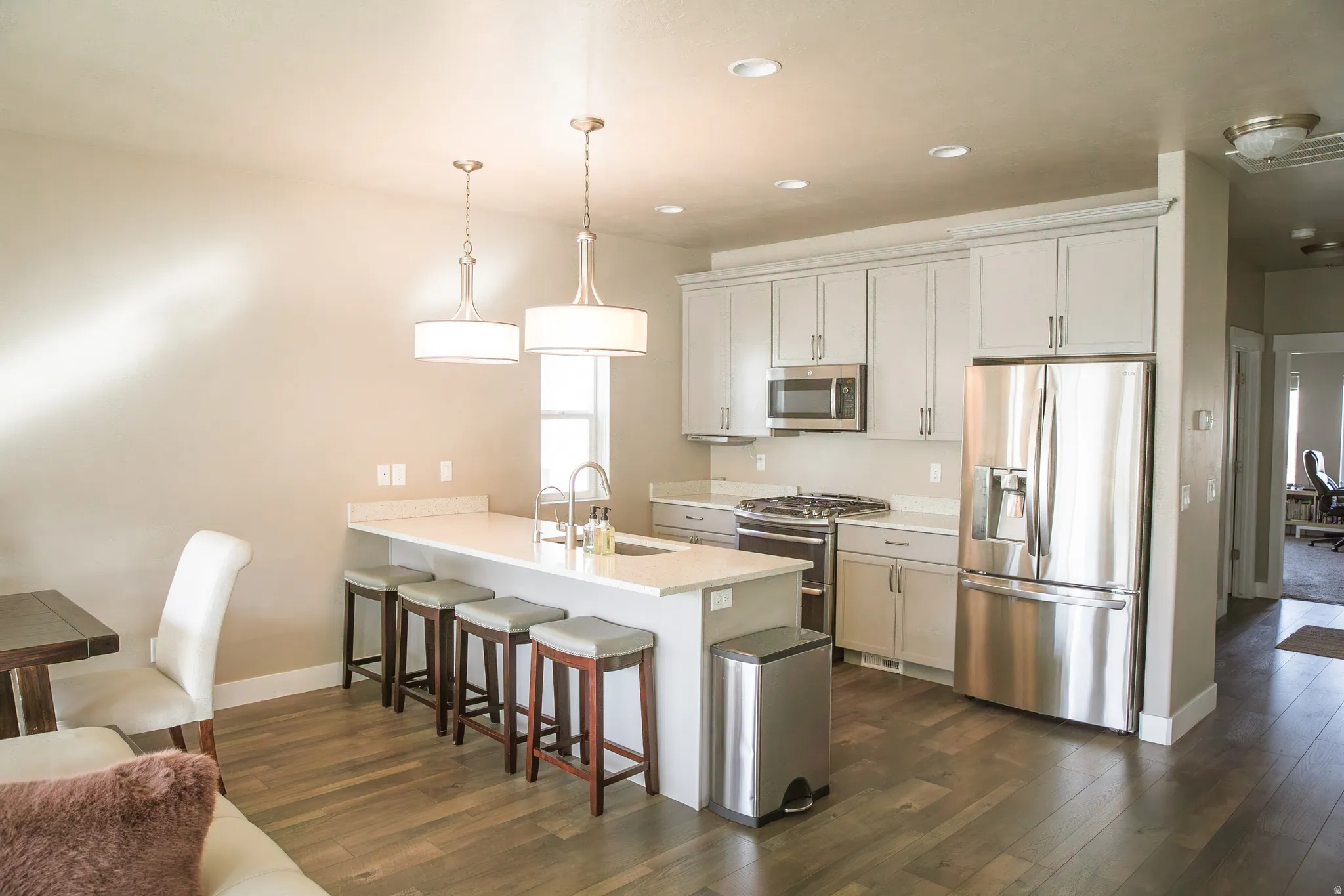 Kitchen with a breakfast bar, stainless steel appliances, a peninsula, dark wood-style floors, and decorative light fixtures