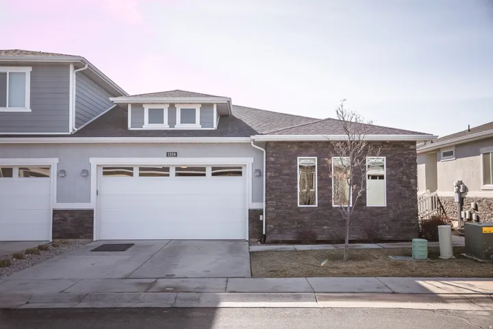 View of front of property with stone siding, concrete driveway, a garage, and roof with shingles