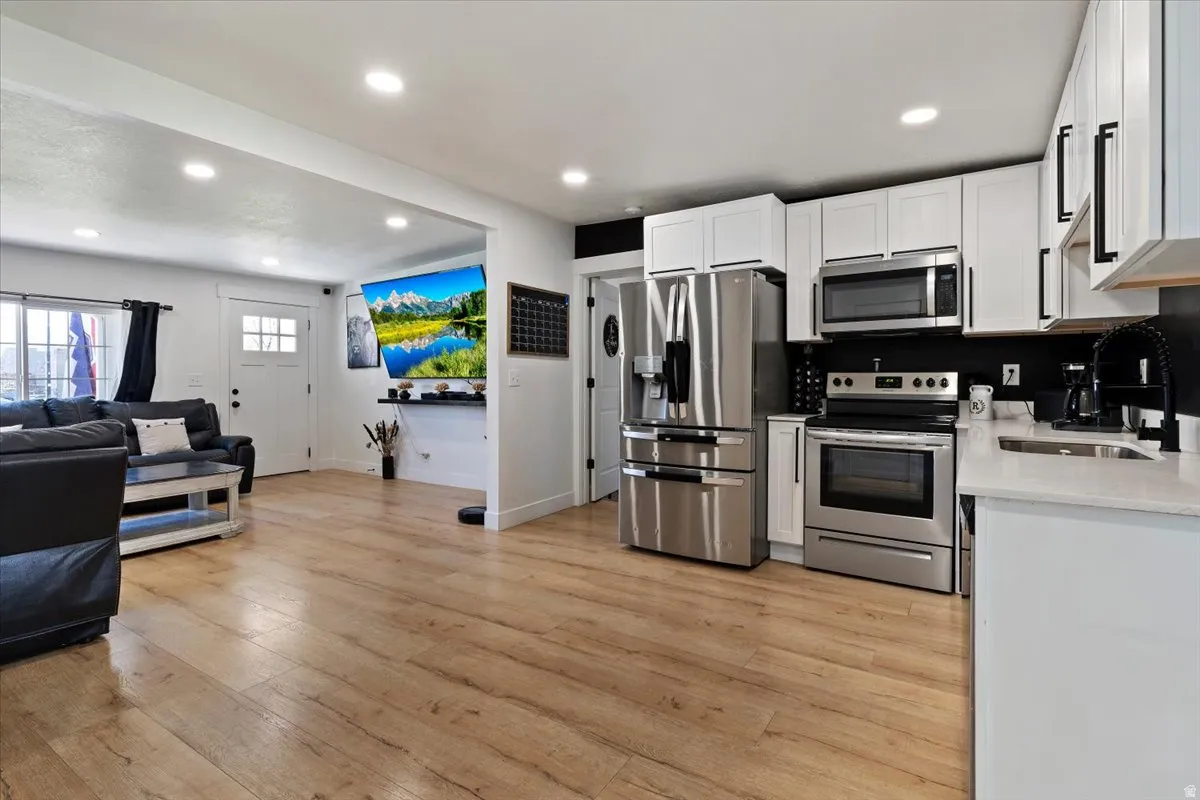 Kitchen featuring stainless steel appliances, open floor plan, recessed lighting, light stone counters, and light wood-style floors