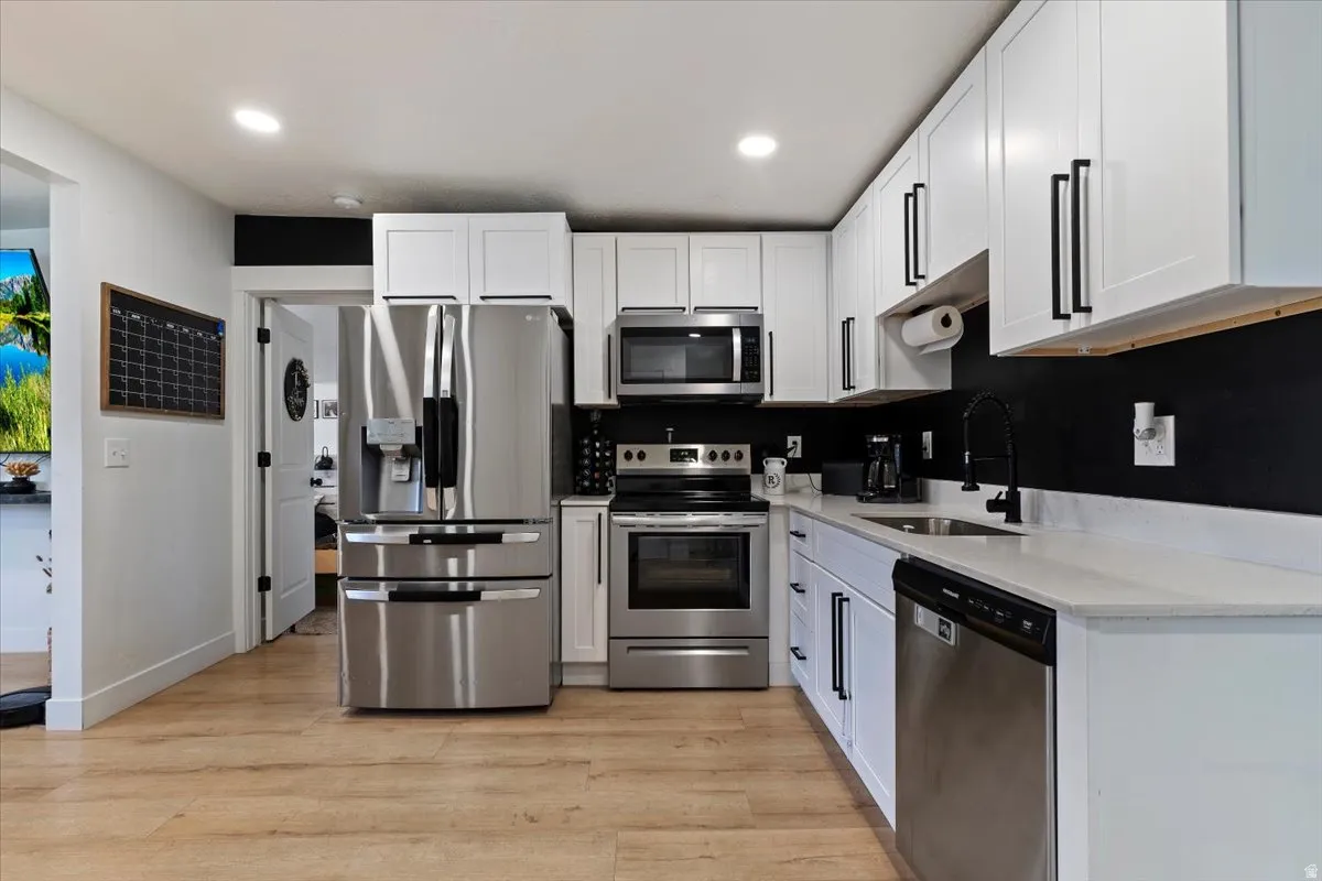 Kitchen with stainless steel appliances, light stone counters, white cabinets, light wood-type flooring, and recessed lighting