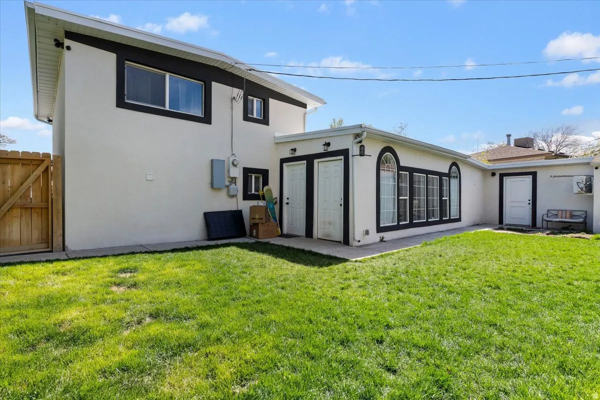 Back of property featuring stucco siding, a lawn, and a gate