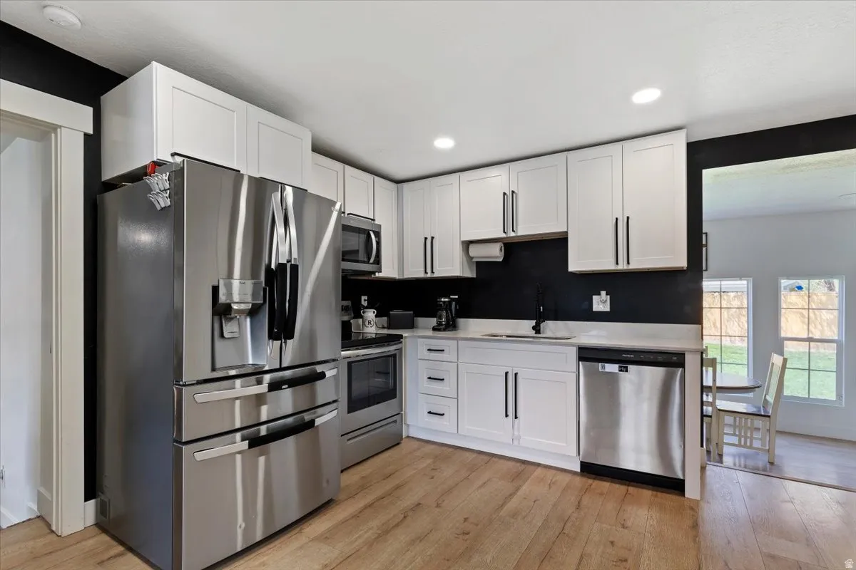 Kitchen with stainless steel appliances, light wood-style floors, white cabinets, and recessed lighting
