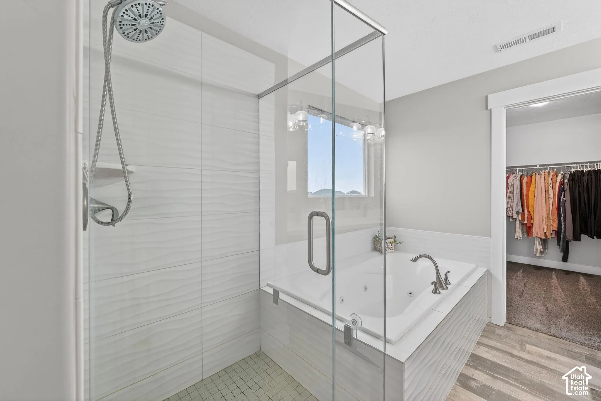 Bathroom featuring a walk in closet, a shower stall, light wood-style floors, and a whirlpool tub