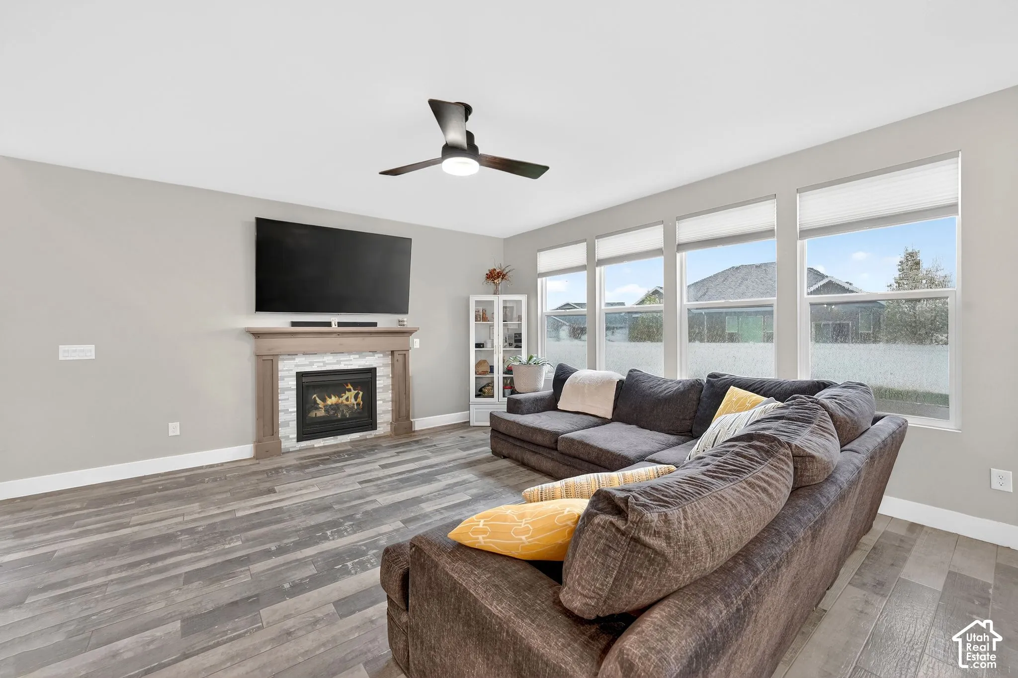 Living room with light wood-type flooring, a ceiling fan, and a warm lit fireplace
