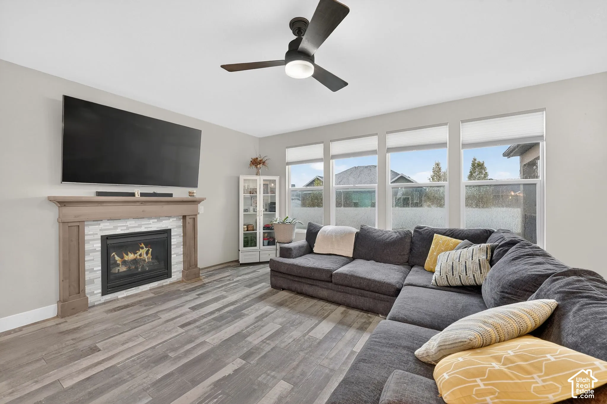 Living area featuring a ceiling fan, light wood finished floors, and a stone fireplace