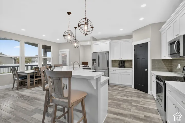 Kitchen with stainless steel appliances, a kitchen breakfast bar, white cabinetry, decorative backsplash, and an island with sink
