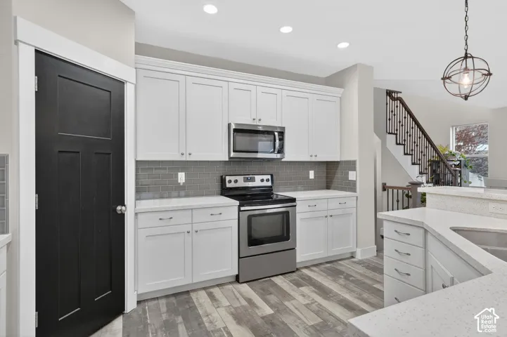 Kitchen with stainless steel appliances, white cabinets, light wood-style floors, decorative backsplash, and pendant lighting