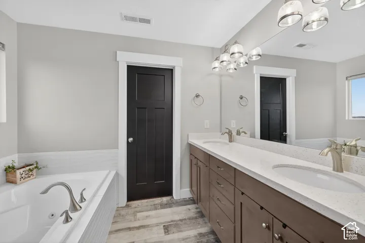 Bathroom featuring a jetted tub, double vanity, and light wood-style floors