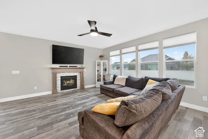 Living room with light wood-type flooring, a ceiling fan, and a warm lit fireplace