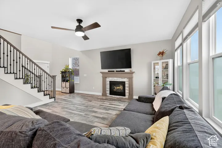 Living room featuring a ceiling fan, wood finished floors, a stone fireplace, and healthy amount of natural light