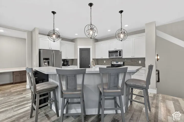 Dual tone kitchen with stainless steel appliances, a kitchen breakfast bar, dual tone cabinetry, backsplash, and a large island