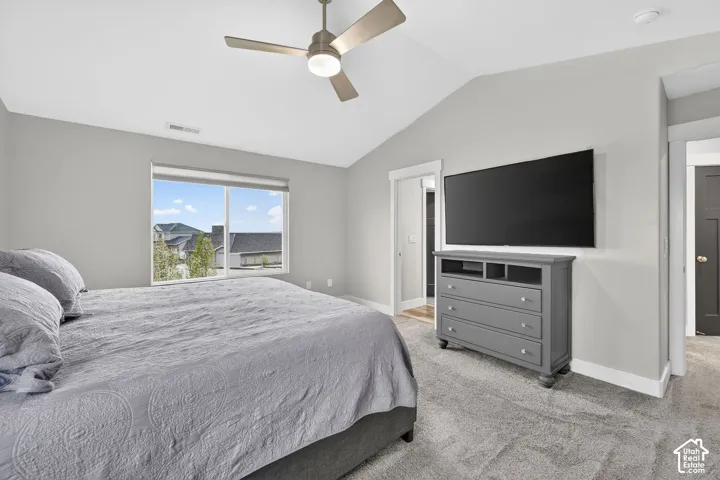 Bedroom featuring vaulted ceiling, light carpet, and a ceiling fan