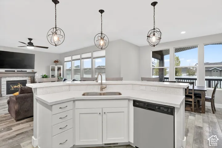 Kitchen featuring white cabinetry, open floor plan, a warm lit fireplace, dishwasher, and light wood-style flooring