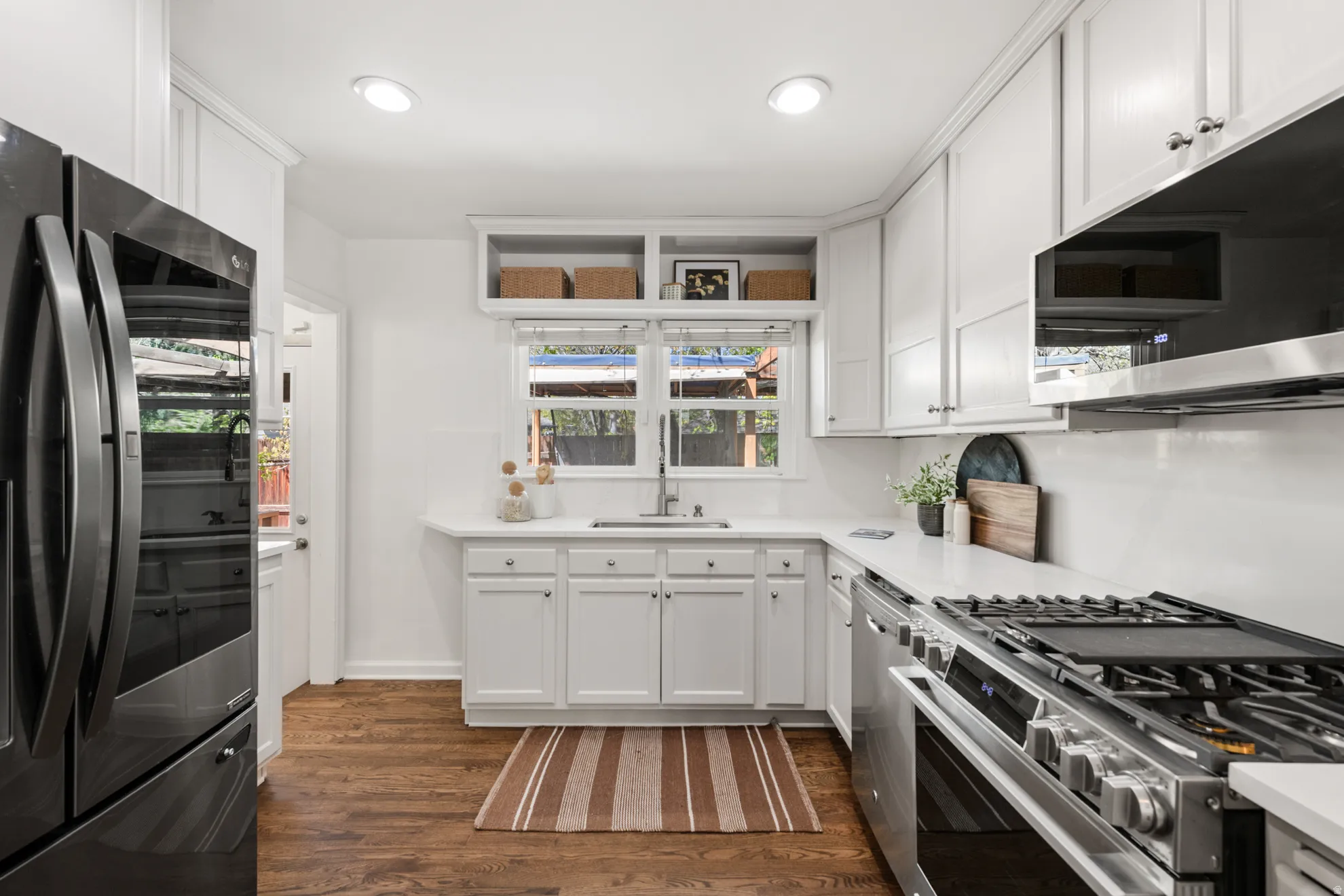 Kitchen with stainless steel appliances, white cabinetry, dark wood-style flooring, recessed lighting, and light stone countertops