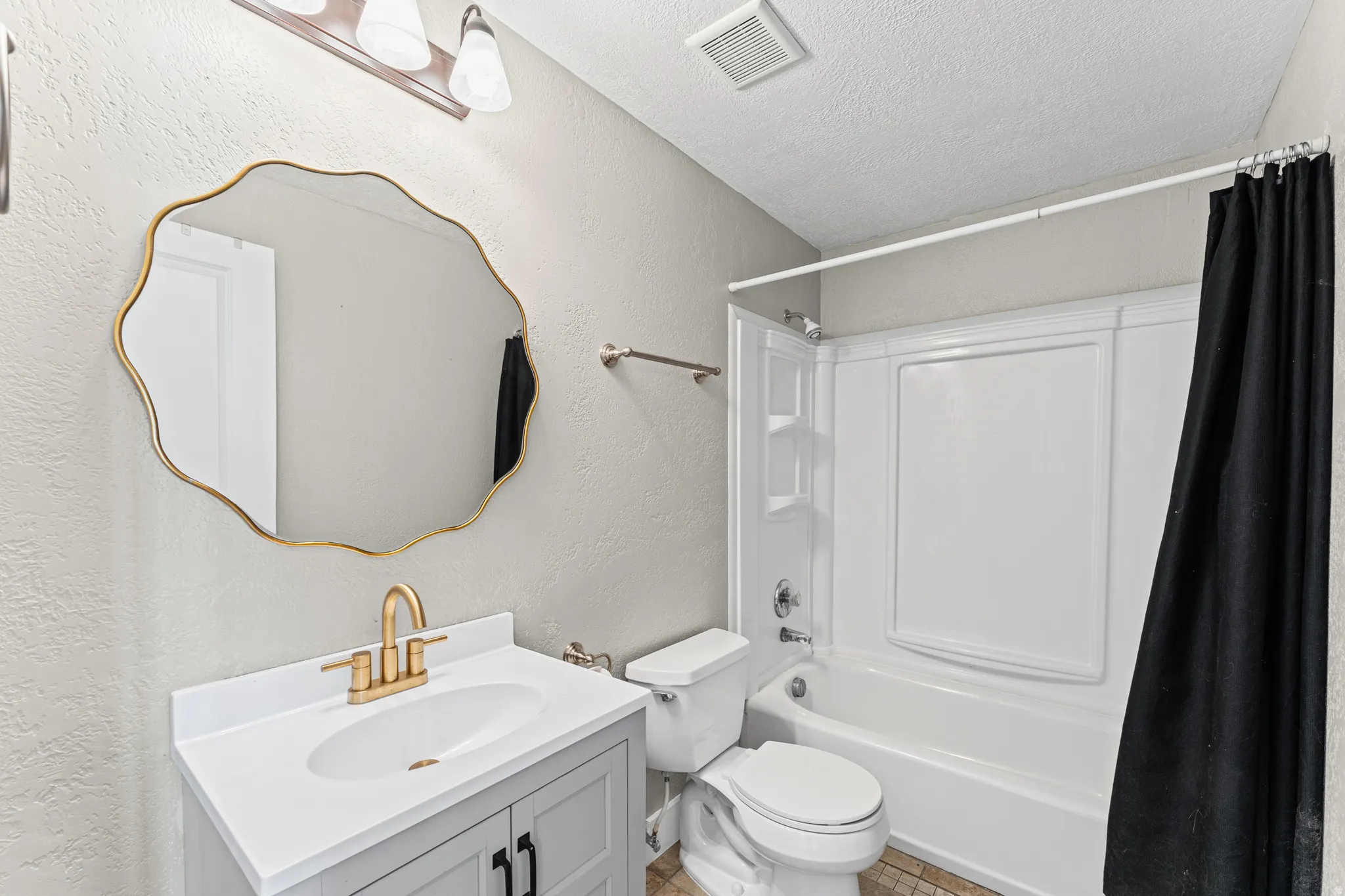 Bathroom with vanity, a textured ceiling, shower / tub combo with curtain, and a textured wall