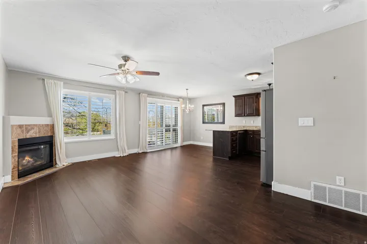 Unfurnished living room featuring dark wood-style flooring, a fireplace, ceiling fan, and plenty of natural light