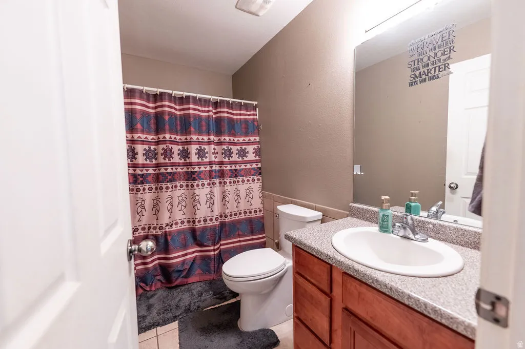 Bathroom with vanity, curtained shower, light tile patterned floors, a textured wall, and wainscoting