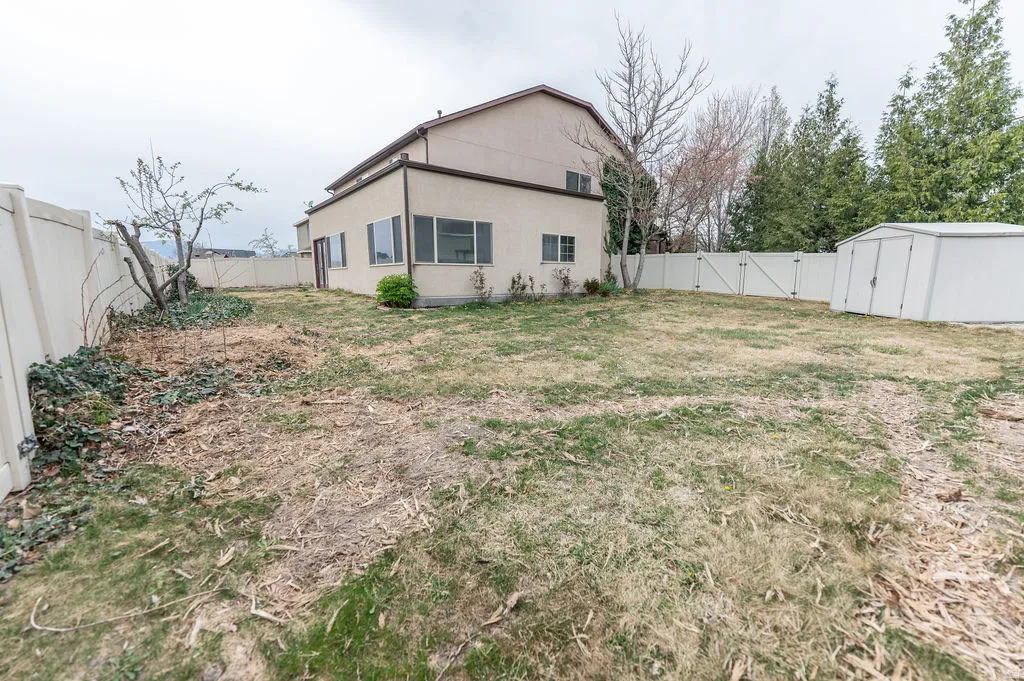 Back of house with a gate, a fenced backyard, stucco siding, and a storage unit
