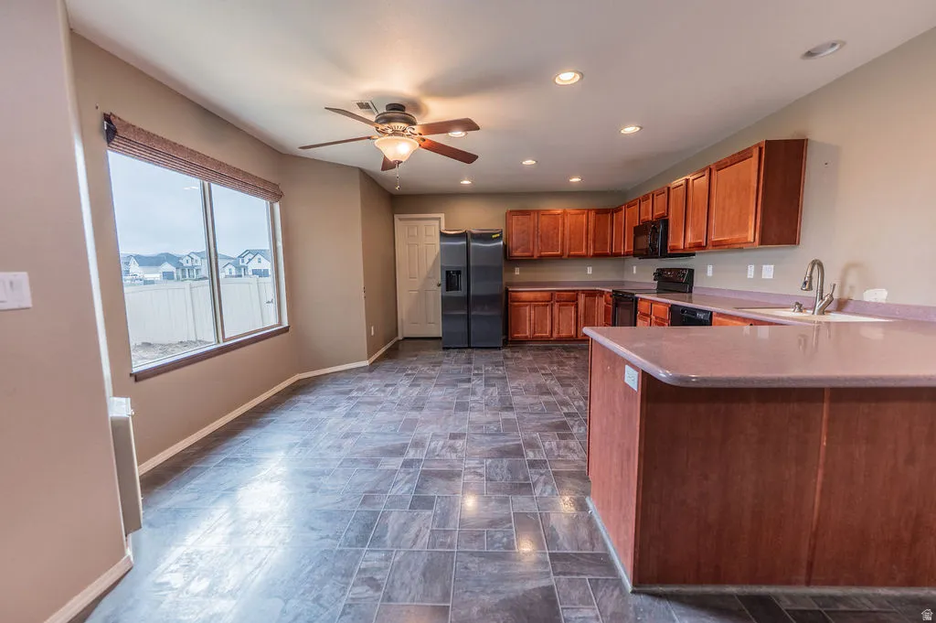 Kitchen with wood finish cabinetry, black appliances, a ceiling fan, a peninsula, and stone finish flooring