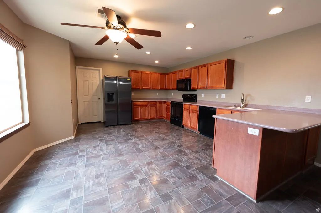 Kitchen featuring light countertops, black appliances, wood finish cabinetry, stone finish flooring, and a peninsula
