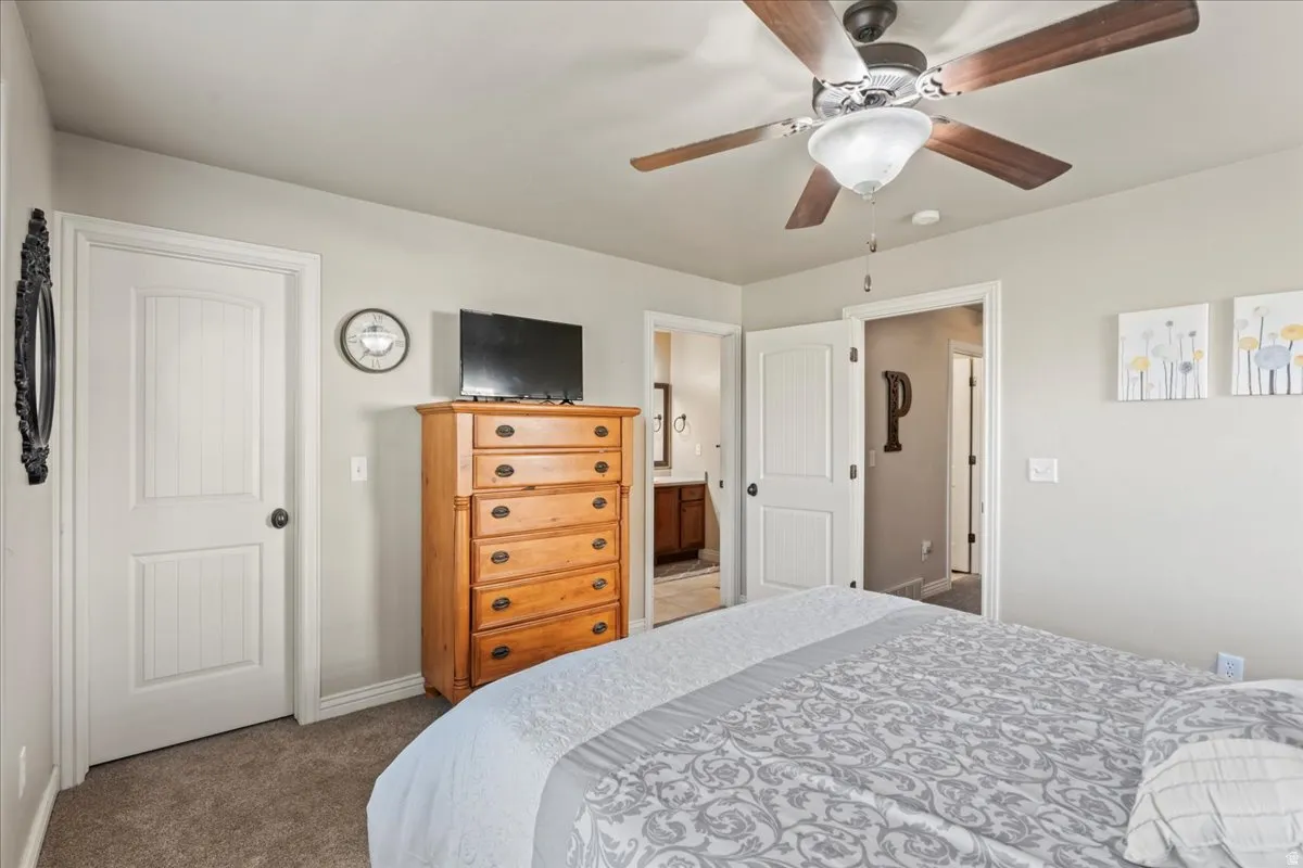 Bedroom featuring dark colored carpet, ceiling fan, and connected bathroom