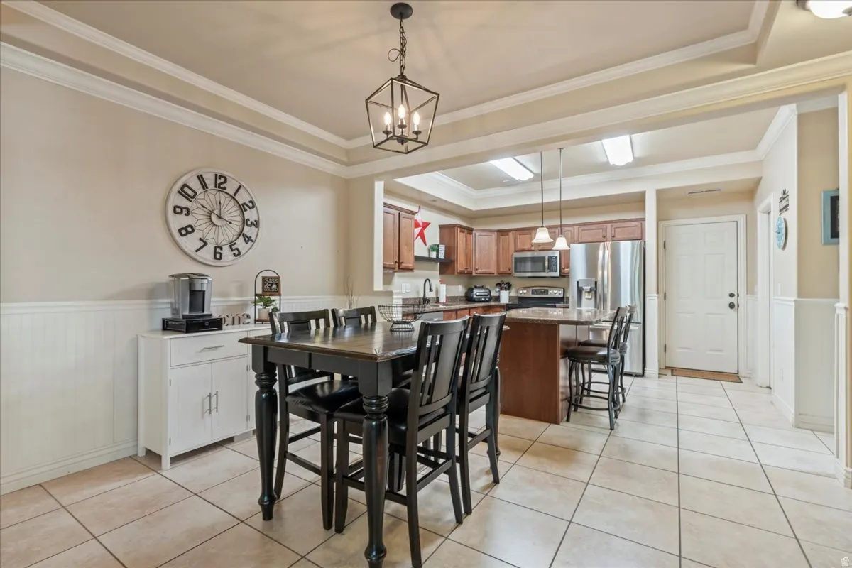 Dining room with a wainscoted wall, hanging lights, ornamental molding, and light tile patterned flooring