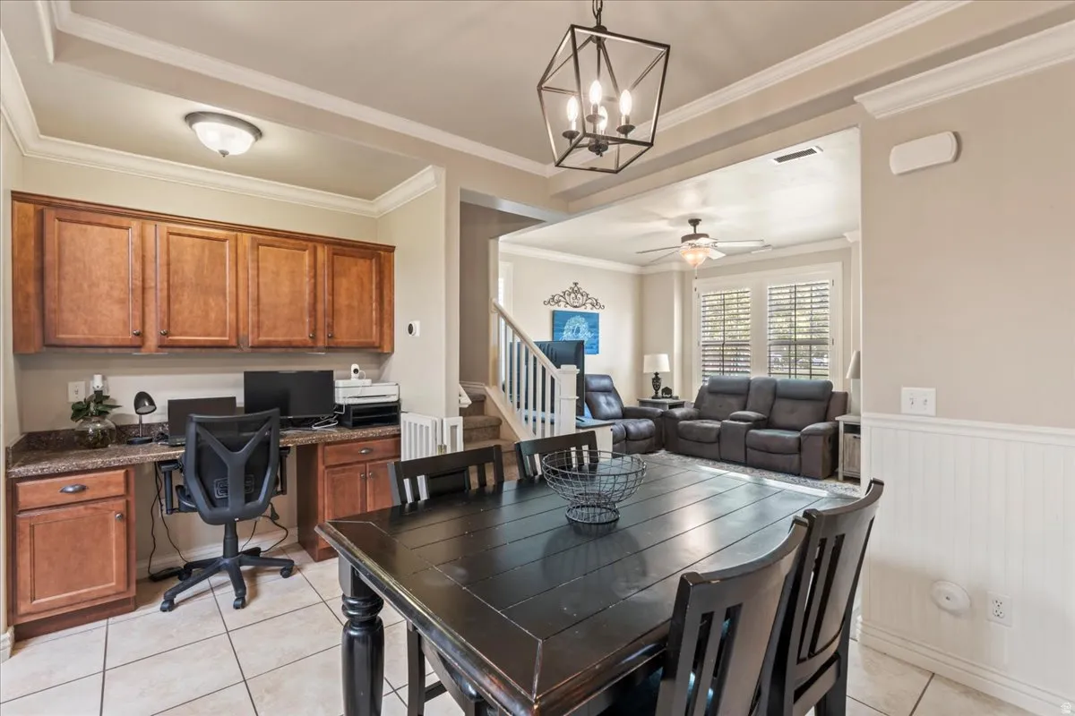 Dining room with built in study area, ceiling fan, ornamental molding, suspended lighting, and light tile patterned floors