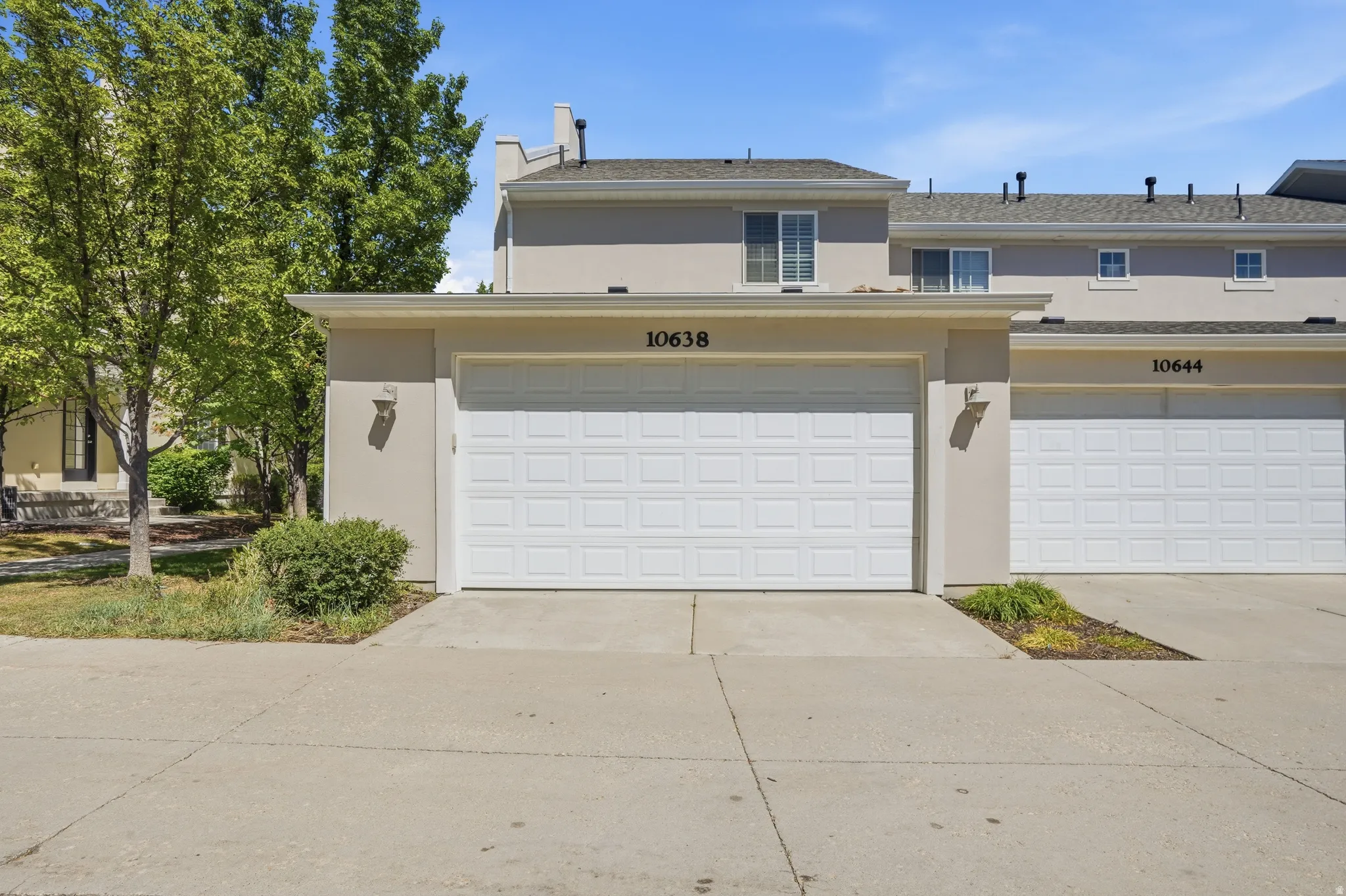 Stucco exterior featuring a prominent two-car garage with white panel doors, accented by an outdoor wall sconce