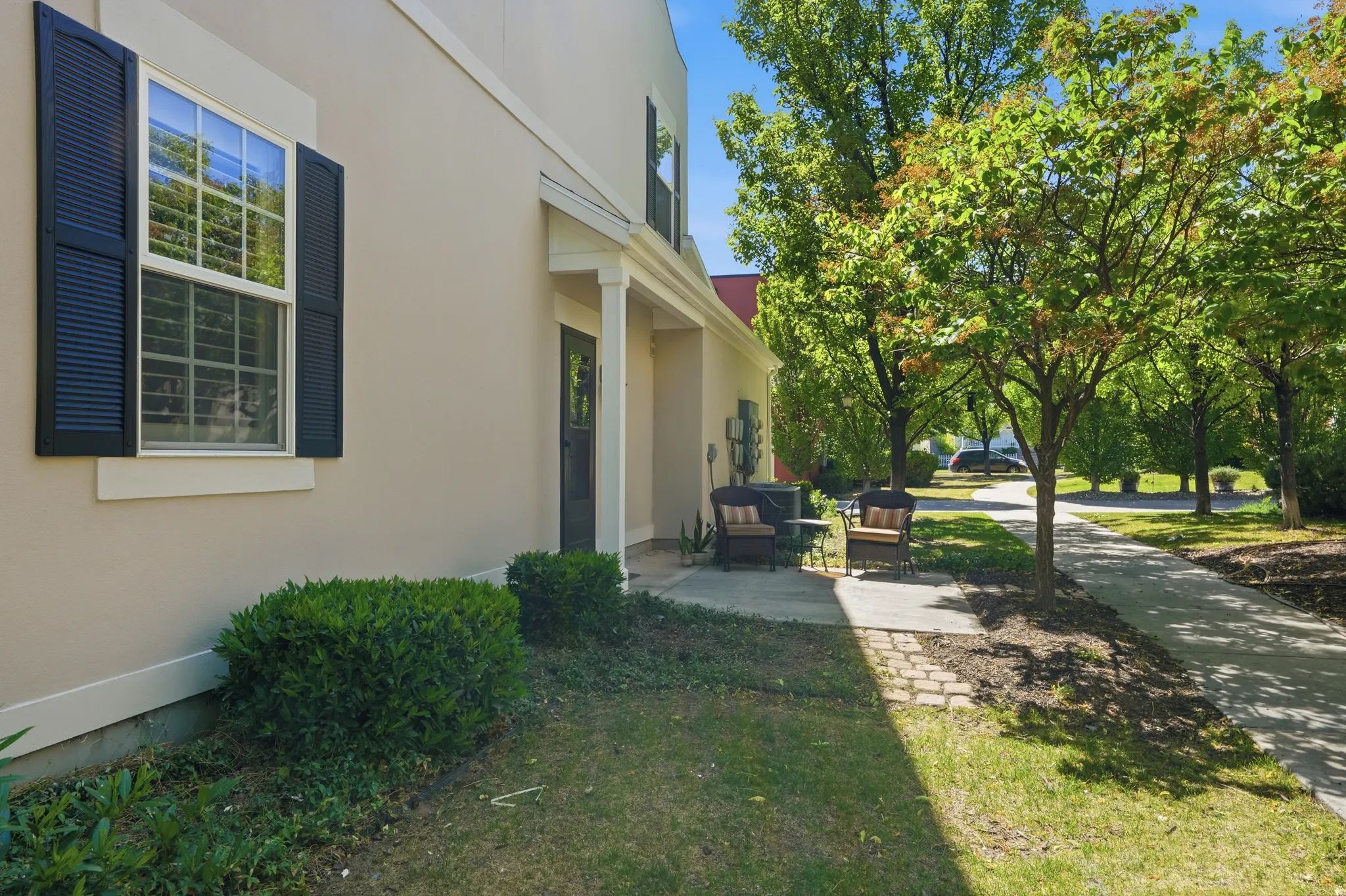 Exterior stucco siding with a covered entryway, black panel shutters, and a front patio with paver accents