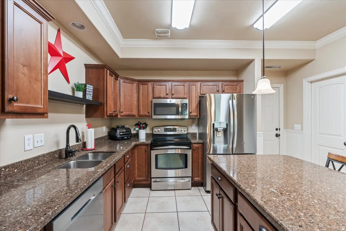 Kitchen with stainless steel appliances, dark stone counters, ornamental molding, decorative light fixtures, and light tile patterned floors