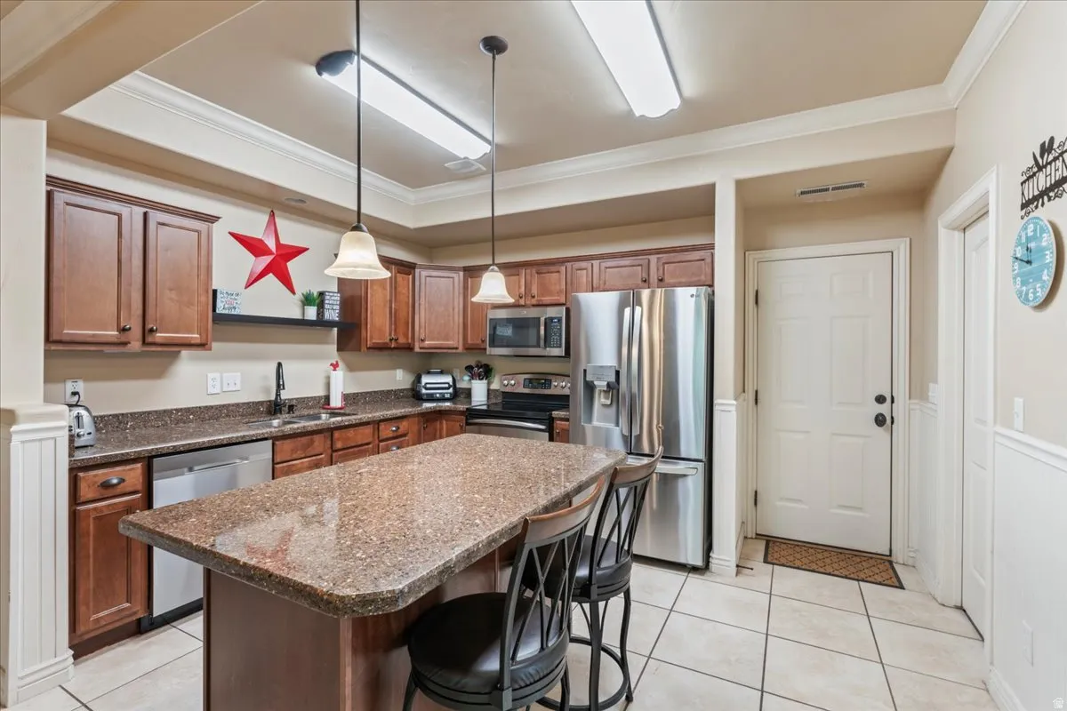 Kitchen with ornamental molding, stainless steel appliances, a center island, a kitchen bar, and hanging light fixtures