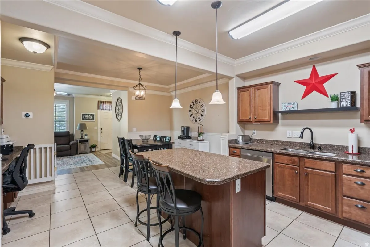 Kitchen featuring a center island, light tile patterned flooring, hanging light fixtures, crown molding, and a breakfast bar