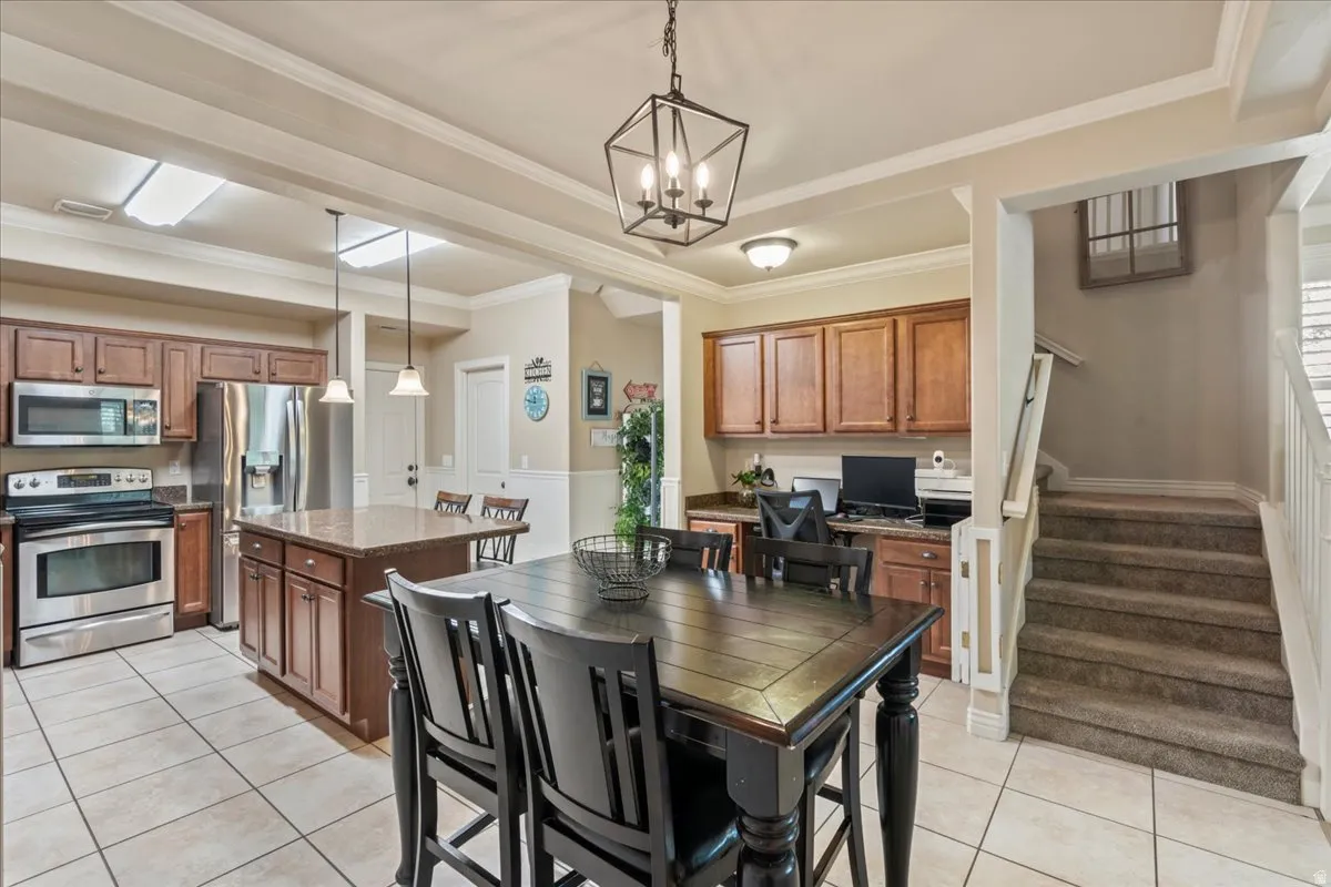 Kitchen featuring stainless steel appliances, wood finish cabinets, a kitchen island, light tile patterned floors, and ornamental molding