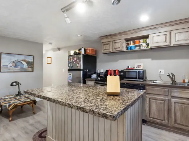 ADU Kitchen featuring a granite-look island with beadboard paneling, L-shaped countertop, wood-finish cabinetry, and wood-finish flooring