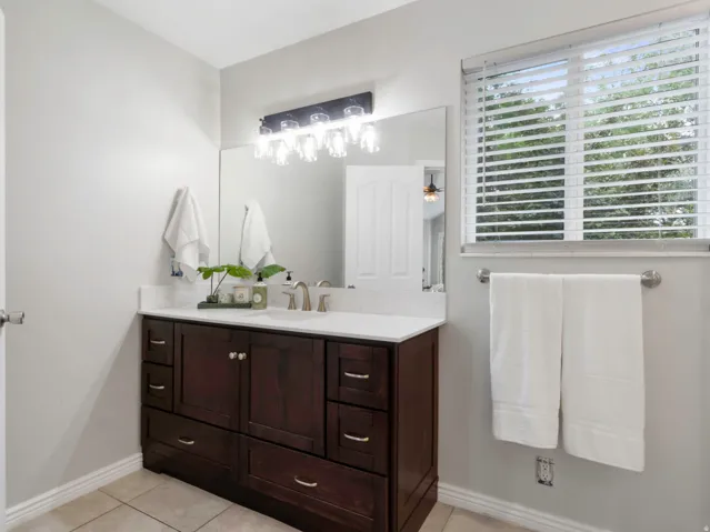 Primary En-suite Bathroom featuring a dark wood double vanity with a white countertop and dual undermount sinks, a large mirror, and a multi-bulb vanity light fixture