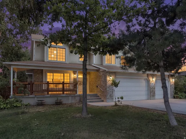 Two-story residence featuring a covered front porch with wood railing, stone accents, two attached garages with carriage-style doors, and a concrete driveway