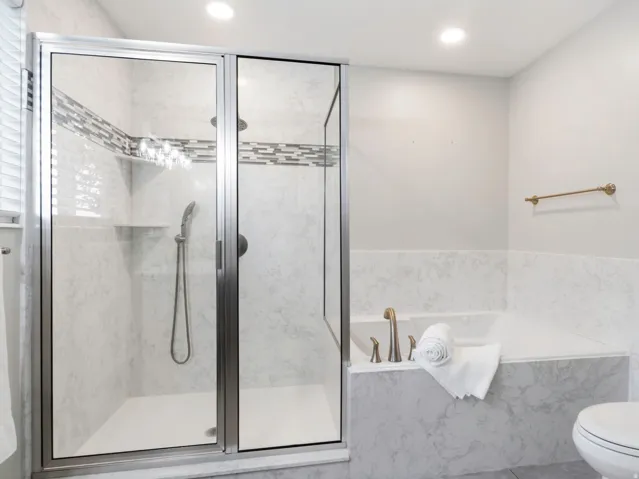 Primary en-suite bathroom with separate soaking tub and glass-enclosed shower featuring a tiled accent band and integrated shelving