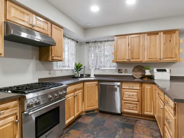 Kitchen featuring wood cabinetry, stainless steel appliances, dark countertops, and slate tile flooring