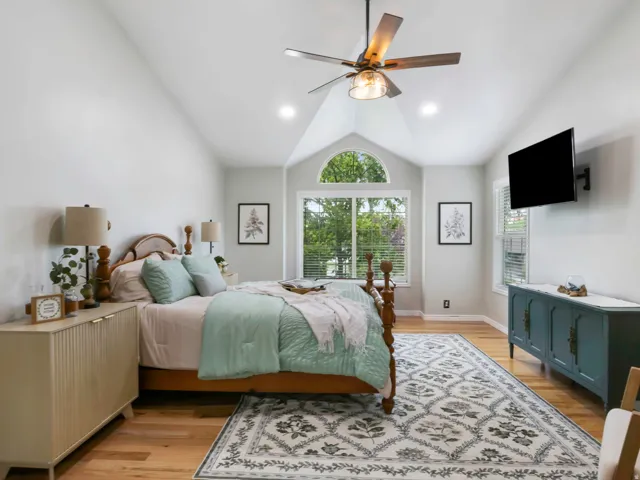 Vaulted ceilings elevate this primary bedroom featuring a large arched window, natural wood-finish flooring, and recessed lighting