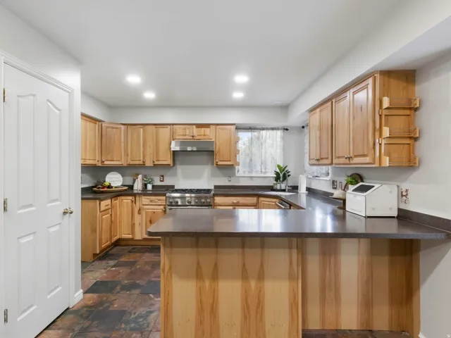 Kitchen featuring wood cabinetry, dark countertops, slate tile flooring, stainless steel range, and recessed lighting