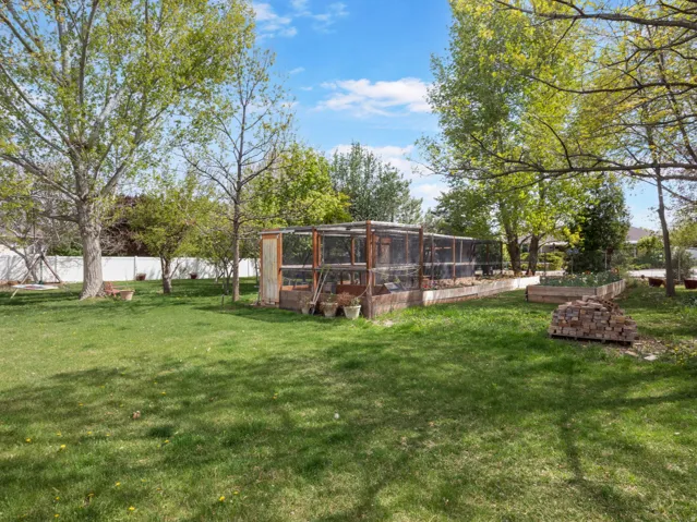 Expansive backyard featuring a large enclosed structure, multiple raised garden beds, mature trees, and a white privacy fence