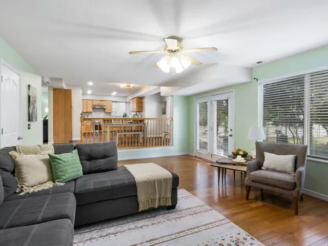Living area featuring wood-finish flooring, light green walls, a ceiling fan, and French doors leading to an outdoor space