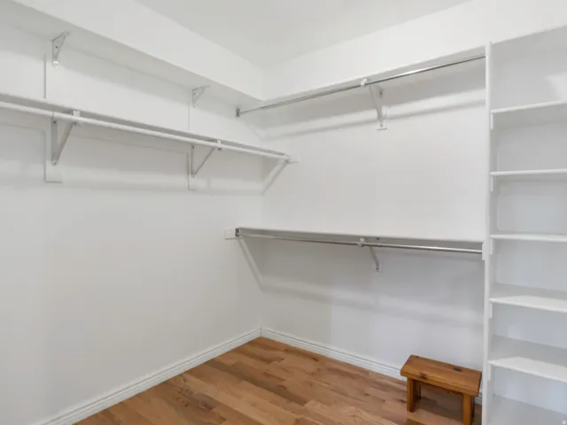 Walk-in primary bedroom closet featuring wood-finish flooring, white walls, multiple hanging rods, and integrated shelving units