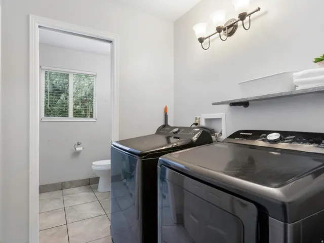 Laundry area featuring a wall-mounted shelf, overhead vanity light fixture, and tile flooring and full hall bathroom.