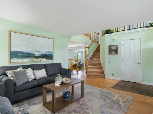 Hardwood flooring throughout the main level featuring a formal entry with tile flooring, a staircase with wood treads and handrails, and an upper-level balcony with black railing