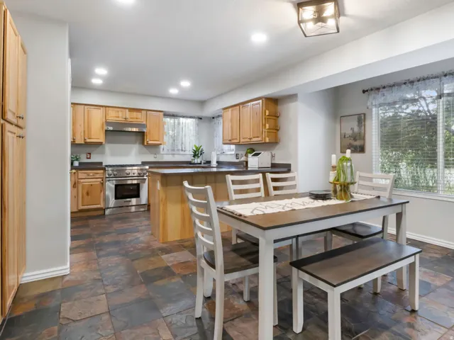 Open-concept kitchen and dining area featuring natural wood cabinetry, dark countertops, stainless steel appliances, and slate-finish flooring